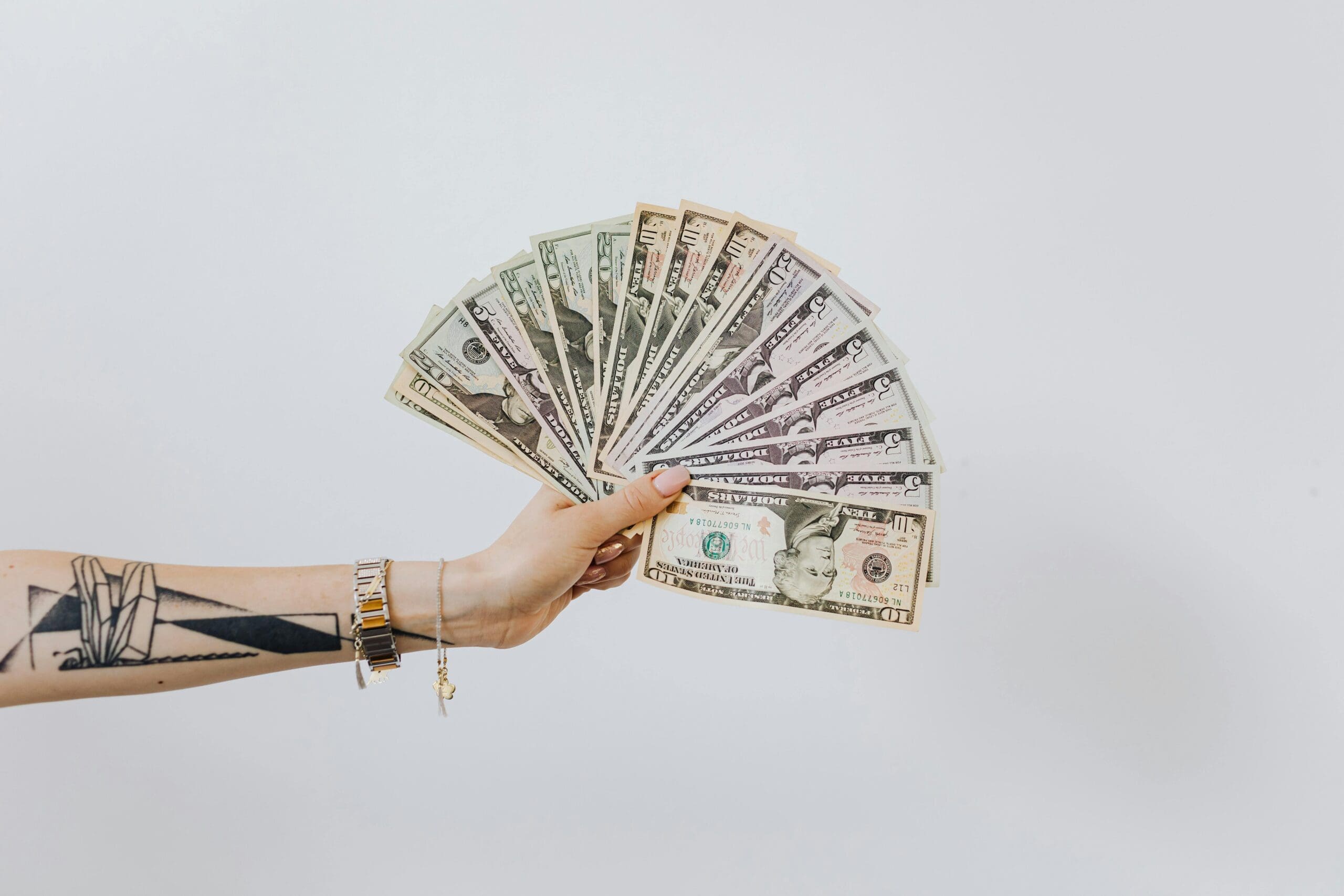A person reaches out their tattooed arm and holds a fan of American dollar bills